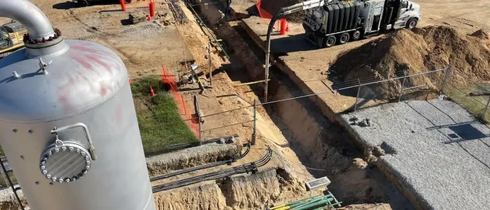 High-angle view of industrial trenching and pipeline work with vacuum truck, storage tank, pipes and excavated dirt